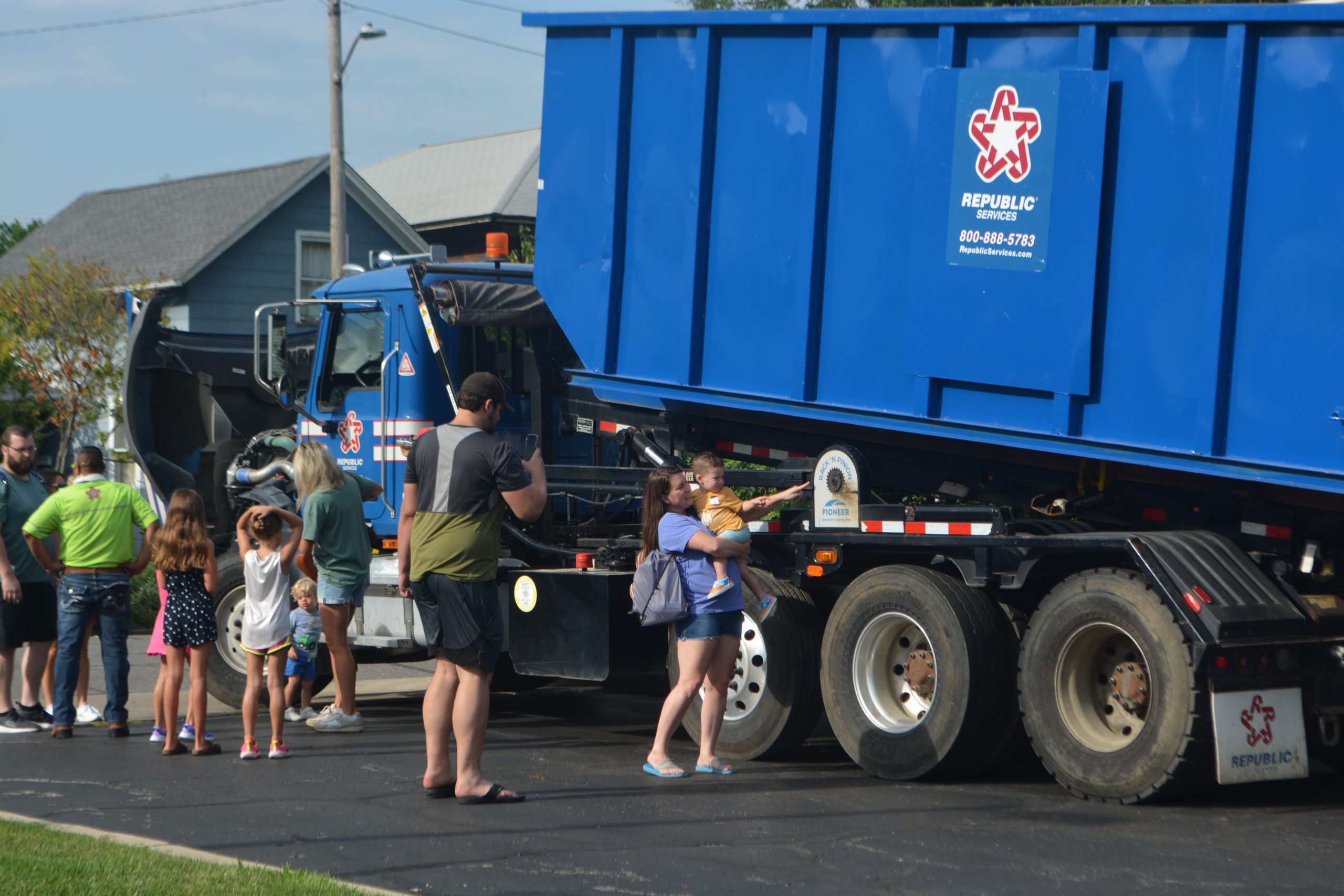 Children and their parents stand next to a dump truck.
