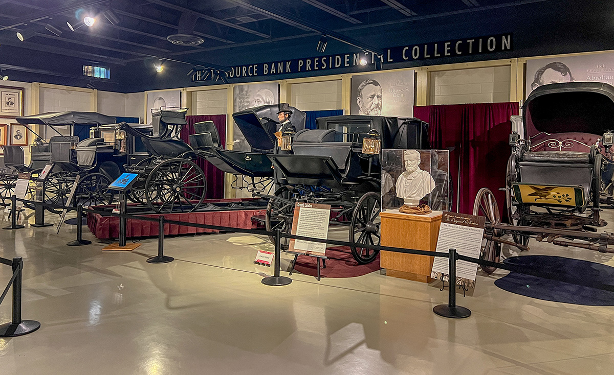 A row of carriages is arranged against some drapes. Stanchions block the carriages.